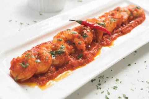Prawns covered in sauce and topped with a red chili on a white plate